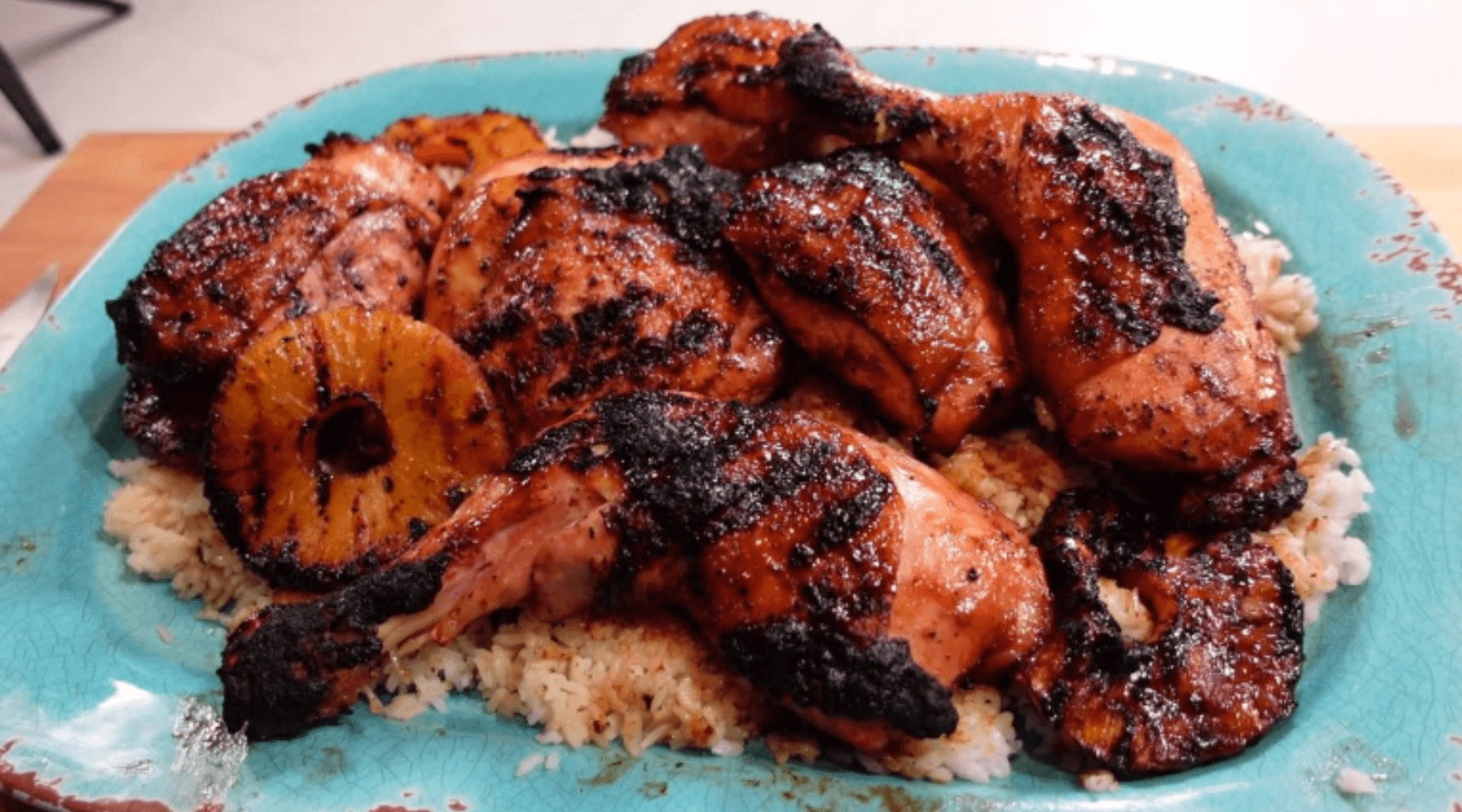 Grilled chicken with char marks served on a bed of rice, garnished with grilled pineapple slices on a turquoise plate.