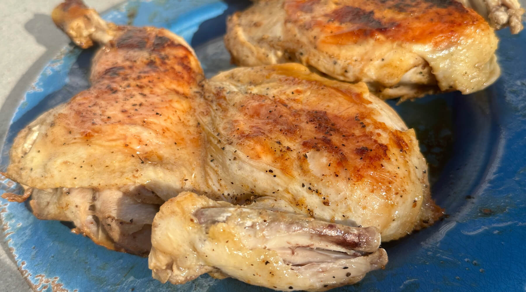 Golden-browned chicken quarters with crispy skin served on a blue plate, cooked using the “under a brick” griddle method.