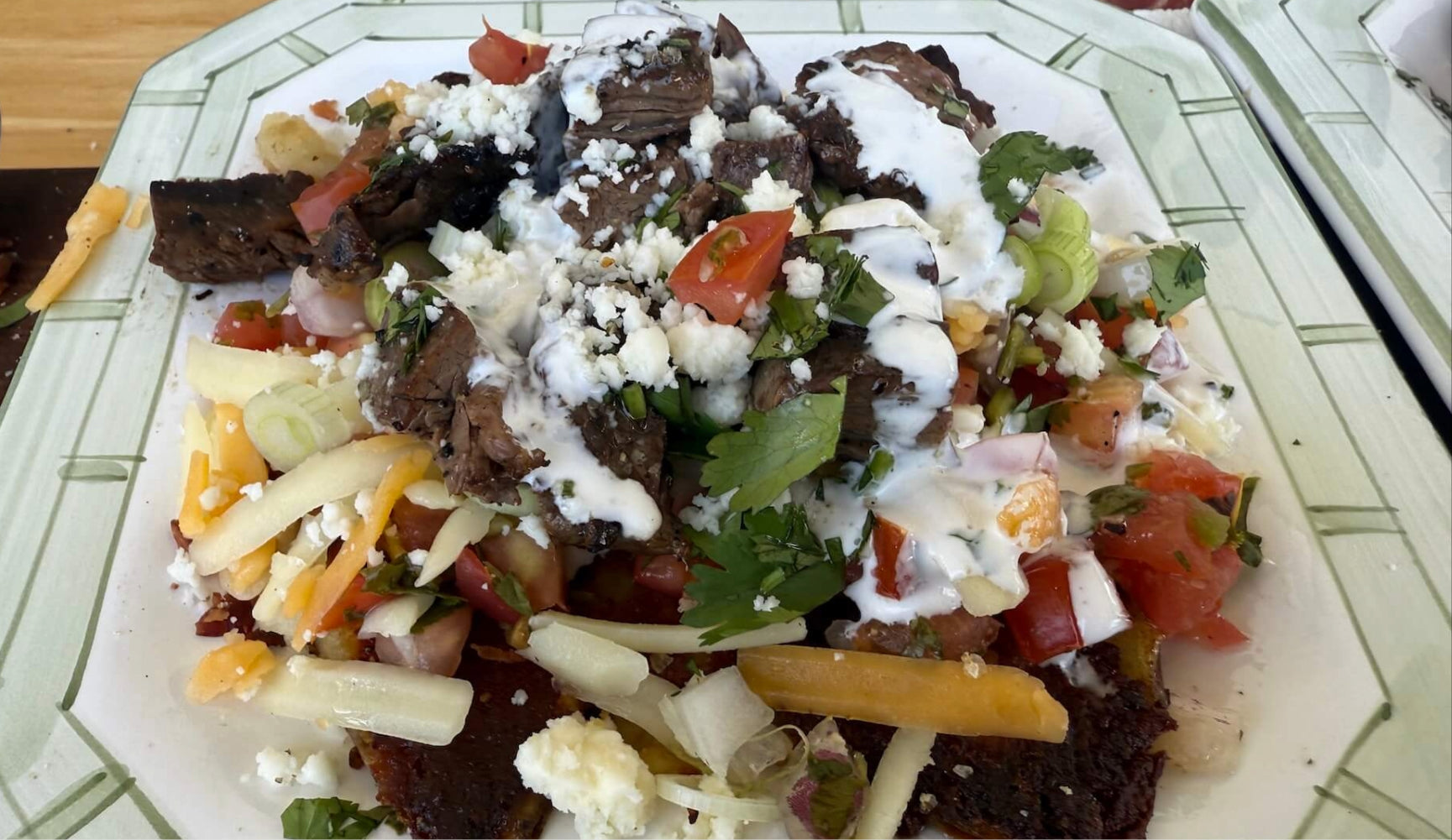 Plate of carne asada fries topped with steak, pico de gallo, cheese, sour cream, and cilantro.