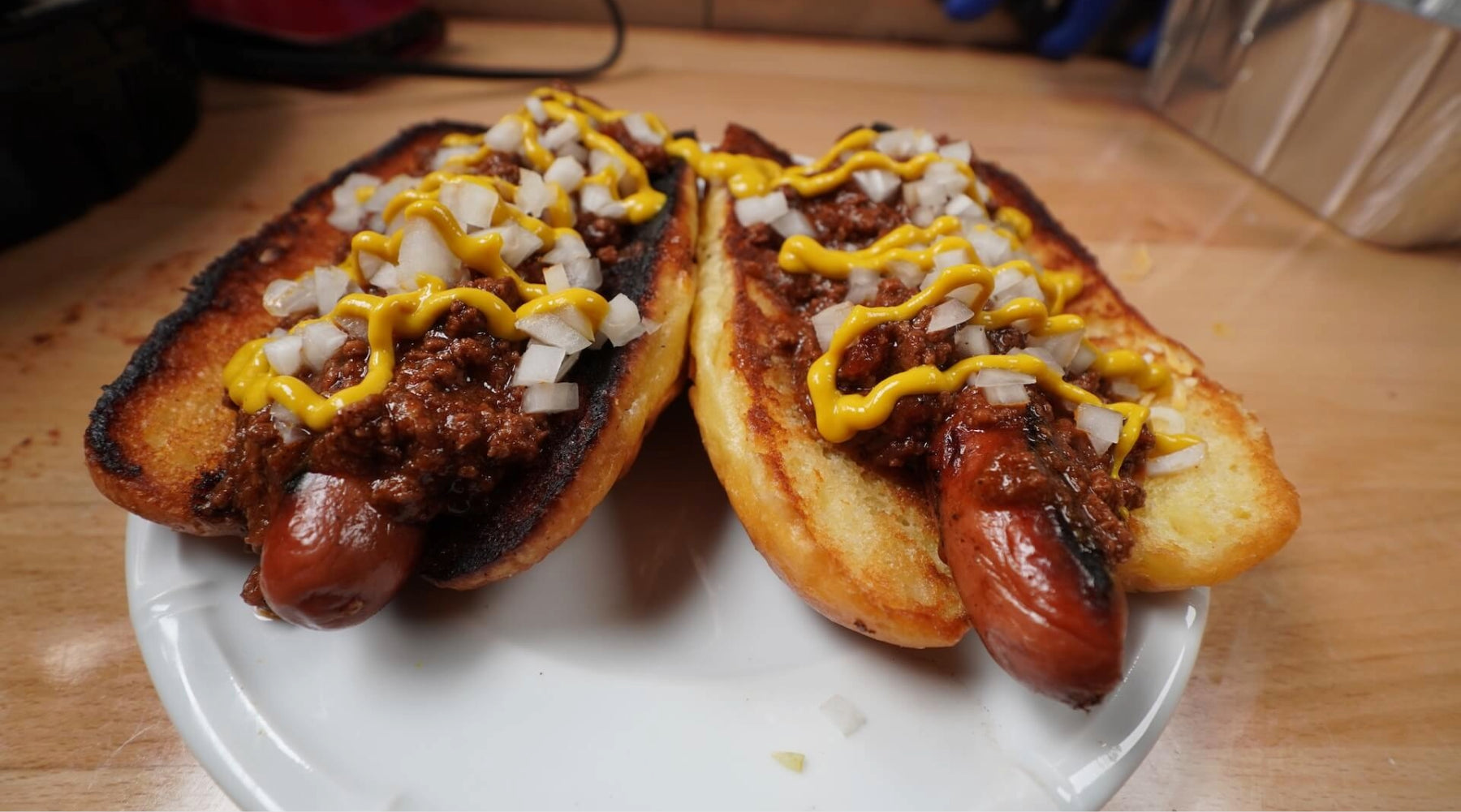 Two chili cheese hot dogs topped with diced onions and mustard on toasted buns, served on a white plate.