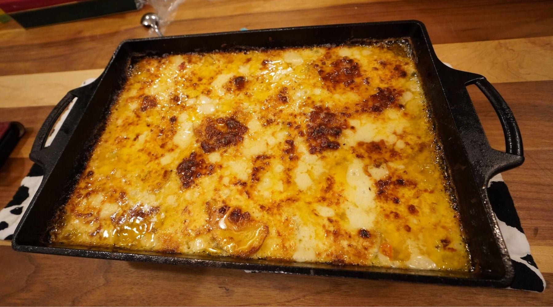 Baked cheesy casserole with a golden, bubbly crust in a rectangular pan on a wooden surface.