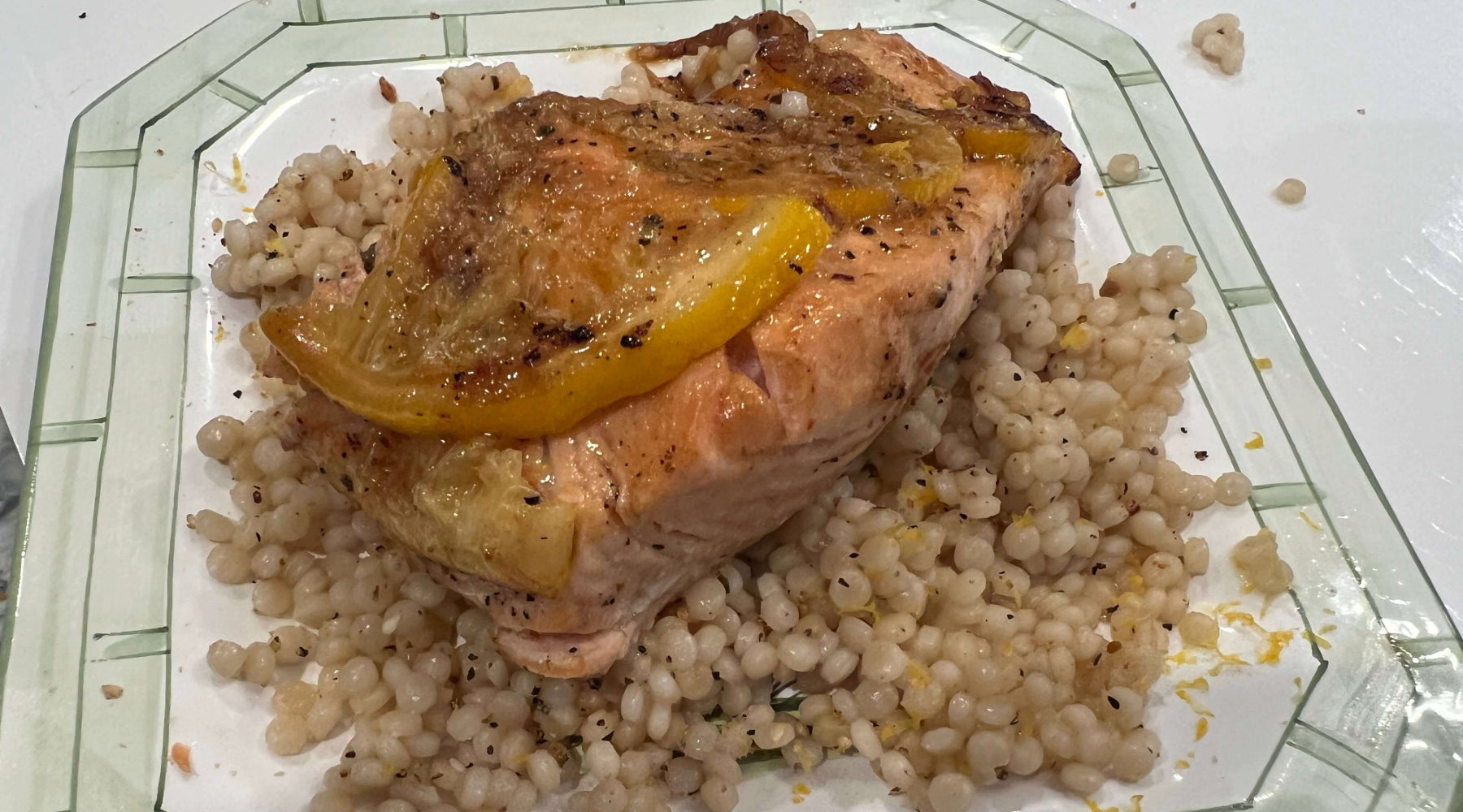 Seared salmon topped with lemon slices, served over pearl couscous with visible seasoning on a plate.