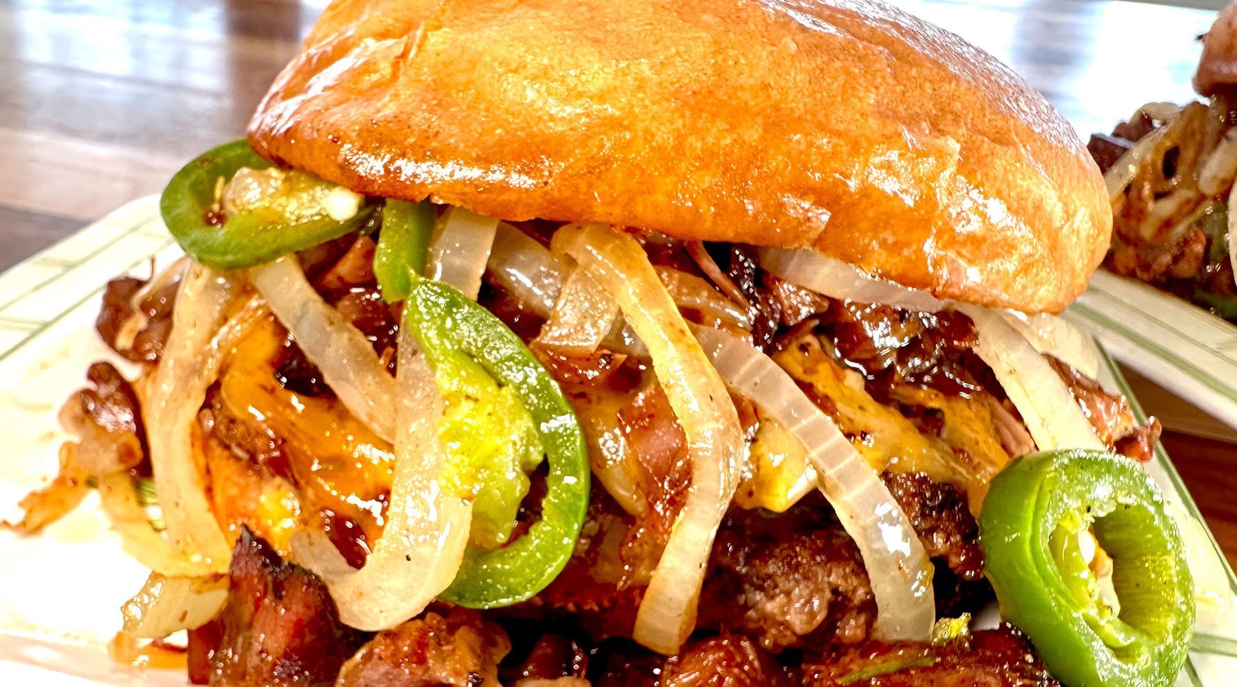 Stacked BBQ sandwich with smash burgers, burnt ends, onions, jalapeños, all topped with Blues Hog Original BBQ Sauce.