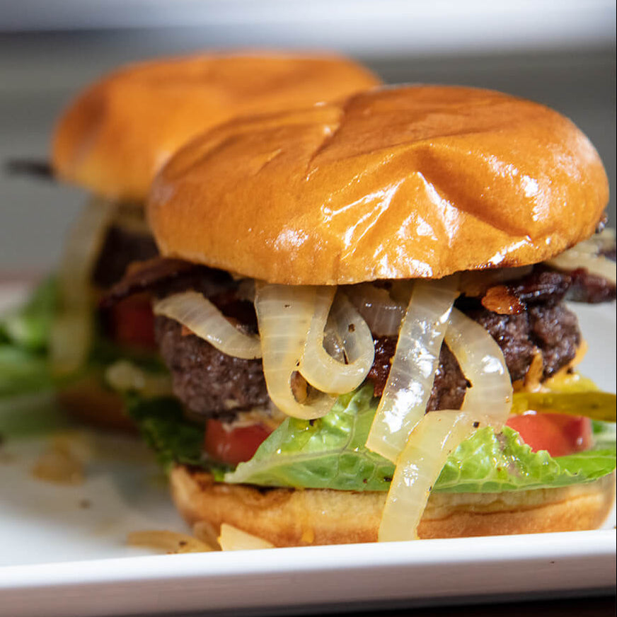 Two burgers with lettuce, tomato, and onions on a white plate.