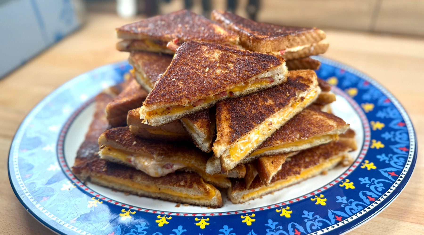 Plate of grilled cheese sandwiches cut into triangles, stacked with melted cheddar between toasted bread.