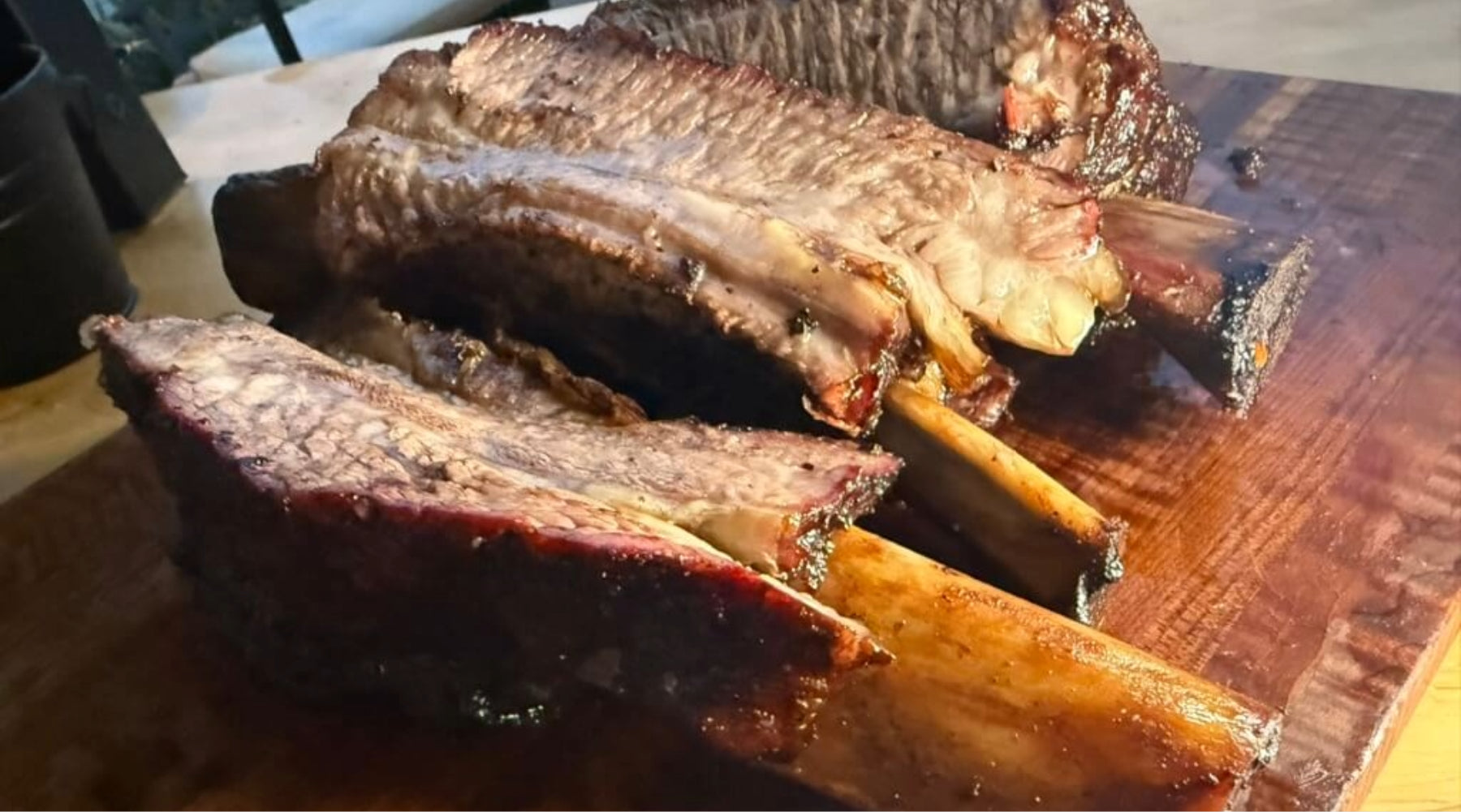 Smoked beef ribs with bark, sliced to show pink smoke ring, resting on a wooden cutting board.