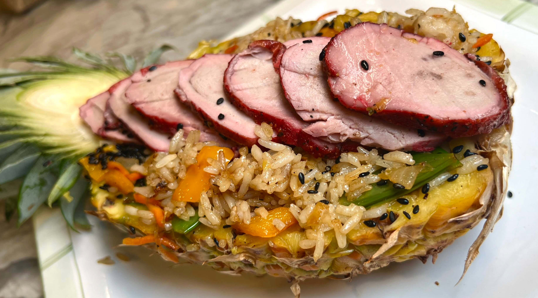 Sliced roasted pork over fried rice with vegetables, served in a hollowed pineapple half and topped with black sesame seeds.