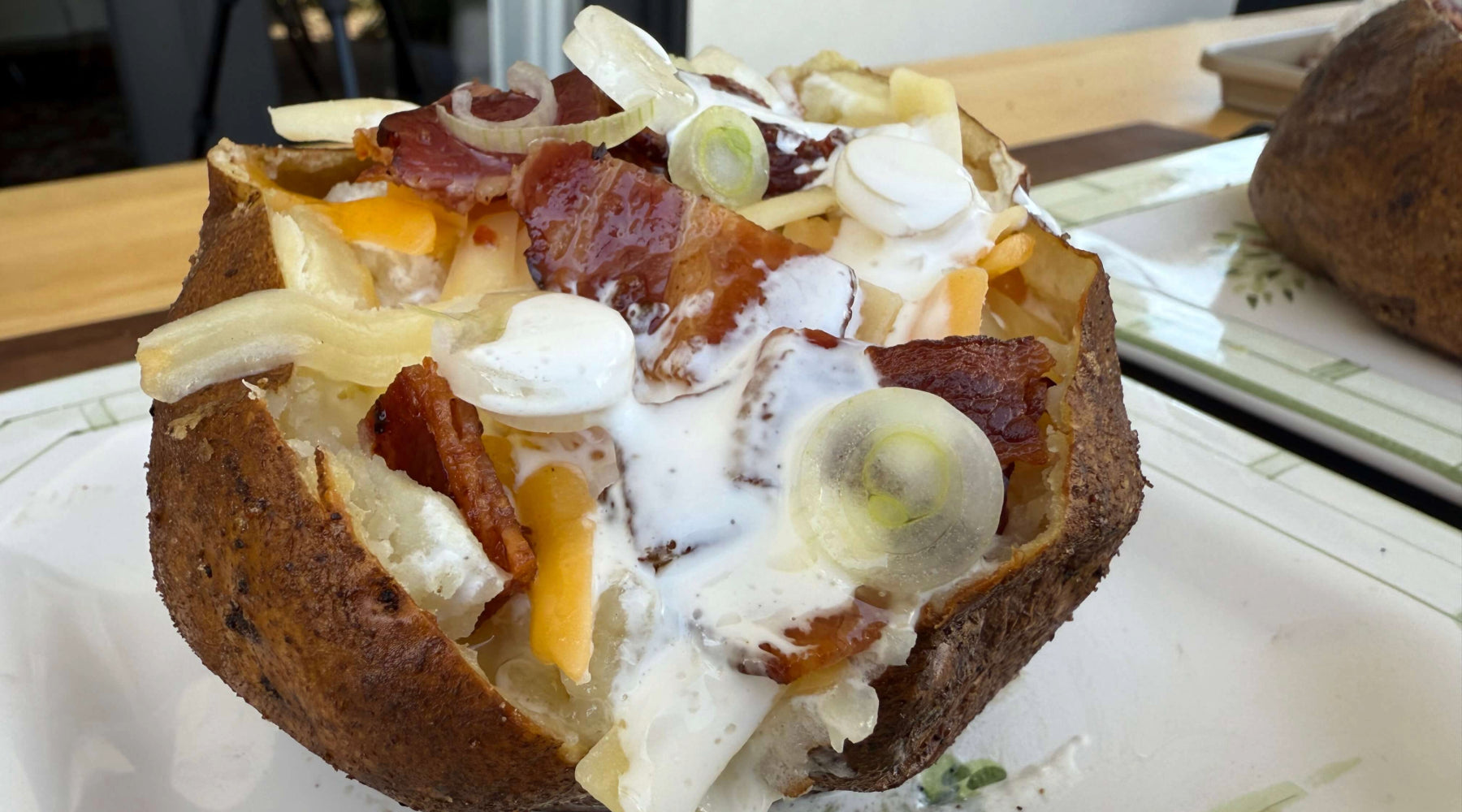 Baked potato stuffed with cheese, bacon, sour cream, and sliced green onions on a plate.