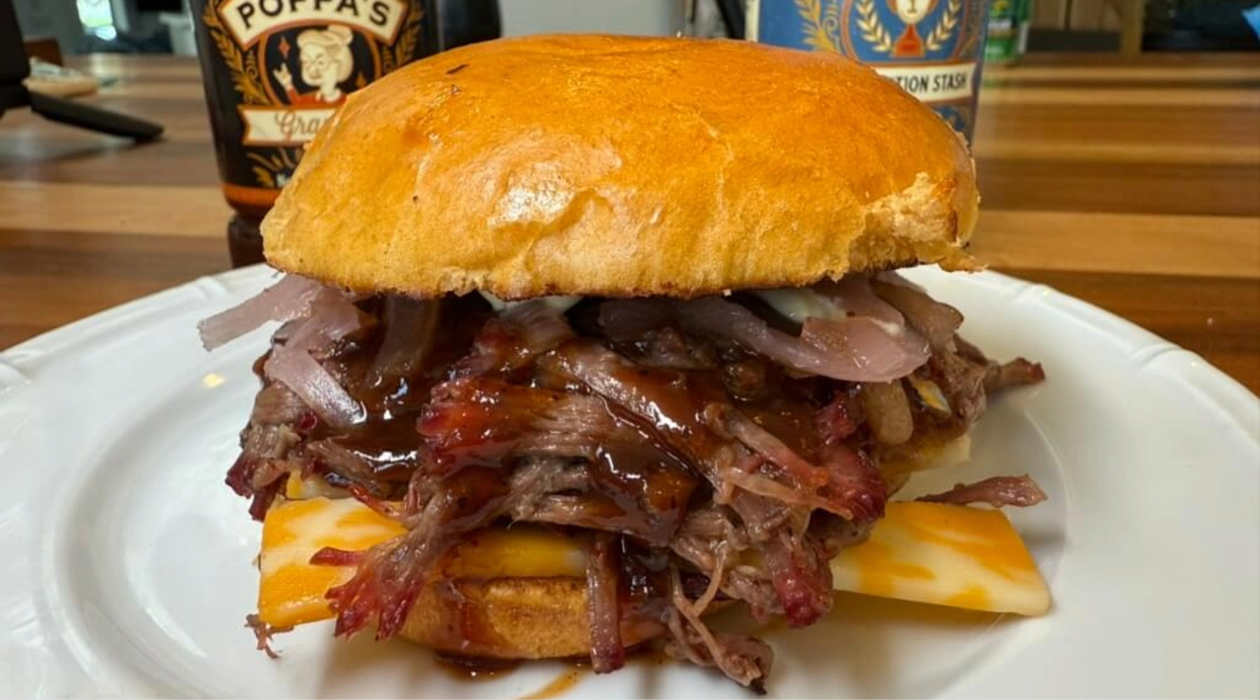 BBQ pulled pork sandwich with melted cheese, onions, and sauce on a toasted bun, served on a plate.