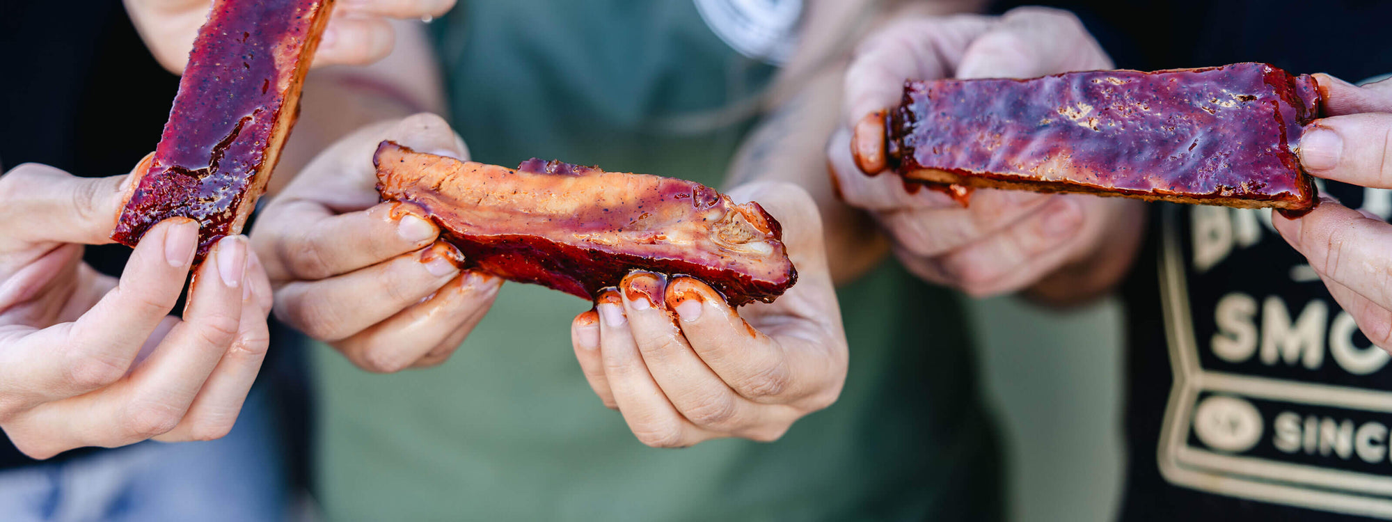 Hands holding slices of smoked meat with a blurred background