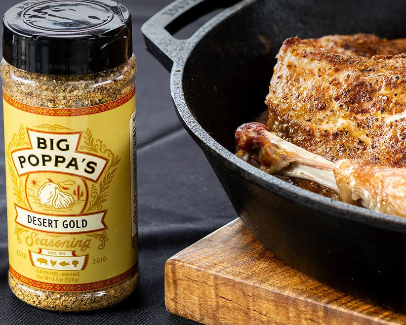 Big Poppa's Desert Gold seasoning bottle next to a skillet with roasted turkey on a dark surface.