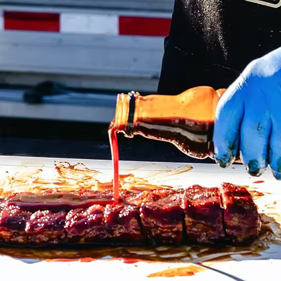 Person pouring barbecue sauce onto ribs with a blurred background